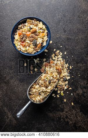 Beakfast cereals in bowl. Healthy muesli with oat flakes, nuts and raisins on black table. Top view.