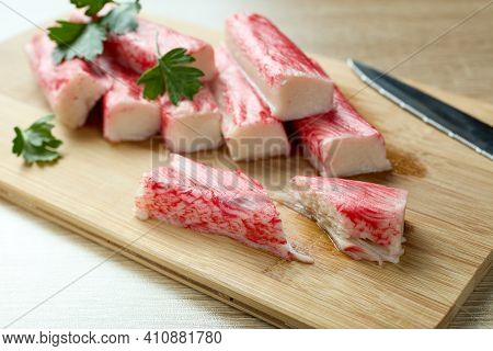 Appetizing crab sticks on wooden cutting board is laying on light table. Selective focus on cut crab stick
