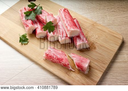 Appetizing crab sticks on wooden cutting board is laying on light table. Selective focus on cut crab stick