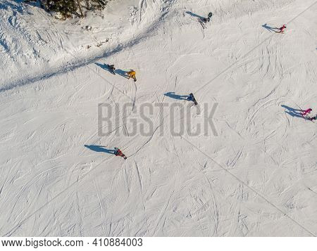 Snowboarders And Skiers Drive Down Ski Slope In Winter Through Fresh Snow, Areal Top View