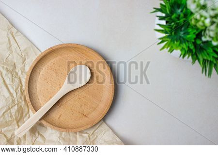 Wooden Utensils On The Kitchen Table. Round Wooden Plate, A Wooden Spoon, A Green Plant. The Concept