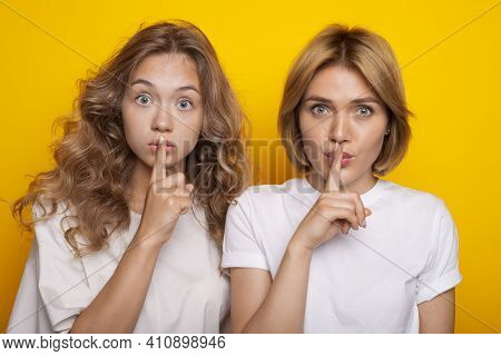 Two Adorable Women With Blonde Hair Are Gesturing At Camera The Silence Sound Posing On A Yellow Stu