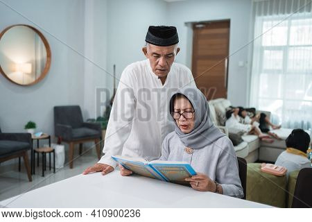 Asian Muslim Senior Man Teaching Wife Reading Koran Or Quran In Living Room