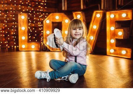 A Little Girl Sits With A Hat On A Background Of Wooden Letters Decorated With Lamps And Smile.