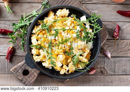 Scrumble Eggs With Corn, Cheese And Arugula On A Wooden Table, Top View. Delicious Homemade Breakfas