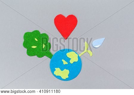 Cutted Out Of Felt The Planet Earth And Tree Waith A Watered Plant Sprout. Copy Space. Gray Backgrou