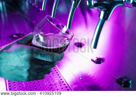 Close-up Beer Glass In Barman Hand In Multicilored Neon Light.