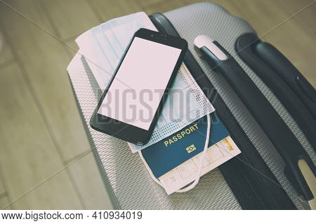 The mobile phone with blank screen as a mockup for digital vaccination certificate iand passport, mask and ticket on the suitcase 