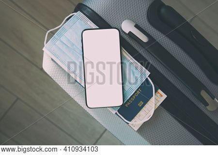 The mobile phone with blank screen as a mockup for digital vaccination certificate iand passport, mask and ticket on the suitcase 