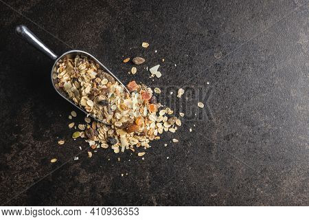 Beakfast cereals in scoop. Healthy muesli with oat flakes, nuts and raisins on black table. Top view.