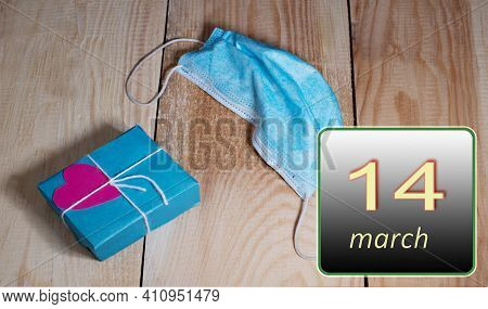 March 14, 14th Day Of Month. Medical Mask From Covid 19 And Box With Gift Lie On Wooden Boards. Spri
