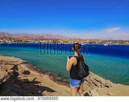 A Tourist Girl With A Backpack And Braided Hair Admires The Seascape In Sharm El Maya Bay (egypt). Y