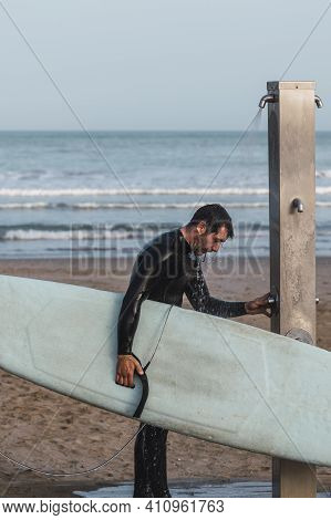 Male Wearing A Neoprene Suit Holding A Surf Board