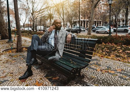 A Gorgeous Mature Dapper Bald Bearded African Businessman In A Neat Formal Suit And Eyeglasses Is Si