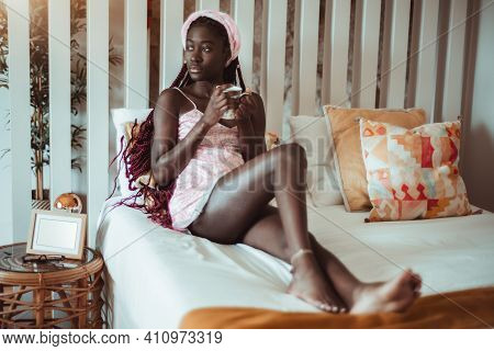 A Pensive Young Sensual Black Barefooted Woman In A Bedgown And With Braids Is Chilling On The Bed I
