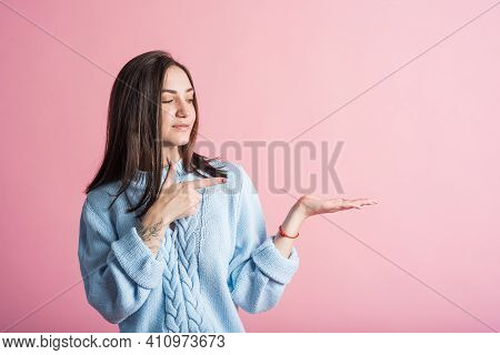 Portrait Of A Brunette Girl Who Points Her Finger At The Palm For Copyspace On A Pink Background