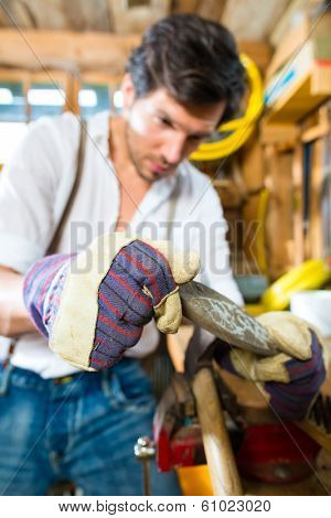 Young man in the Bavarian mountains grinds his axe and sharpening tools with a grindstone to chop the fire wood