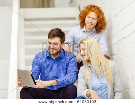 business, technology and startup concept - smiling creative team with tablet pc computer sitting on staircase