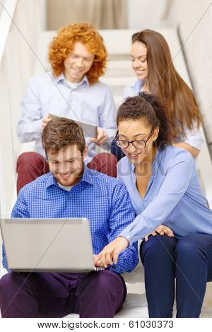 business, technology and startup concept - smiling creative team with laptop and tablet pc computer sitting on staircase