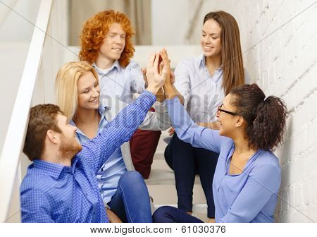 business, office, gesture and startup concept - smiling creative team doing high five gesture sitting on staircase
