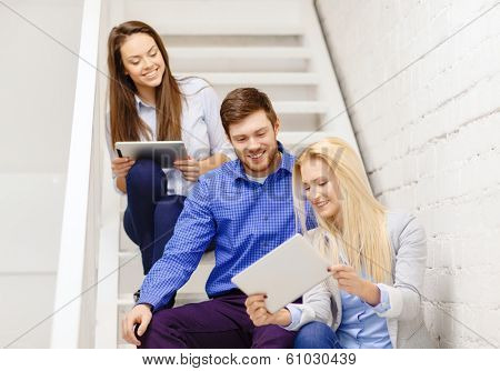 business, technology and startup concept - smiling creative team with tablet pc computer sitting on staircase