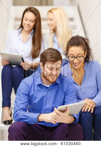 business, technology and startup concept - smiling creative team with tablet pc computer sitting on staircase