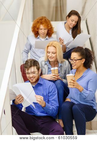 business, office and startup concept - smiling creative team with papers and take away coffee on staircase