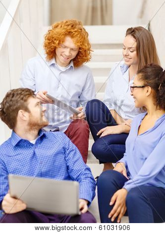 business, technology and startup concept - smiling creative team with laptop and tablet pc computer sitting on staircase