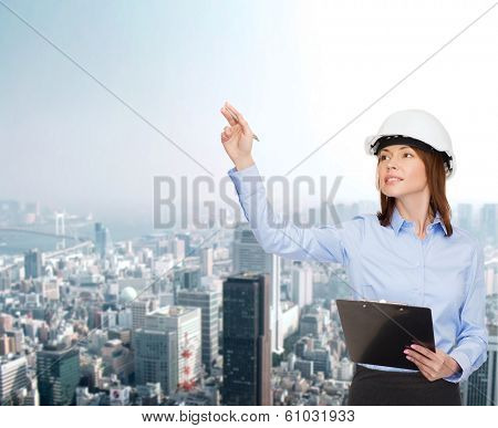 building, developing, consrtuction and architecture concept - smiling businesswoman in white helmet with clipboard pointing finger