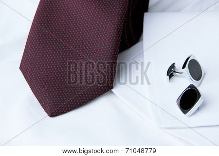 A pair of cuff links on a sleeve of the white shirt and a cravat near it
