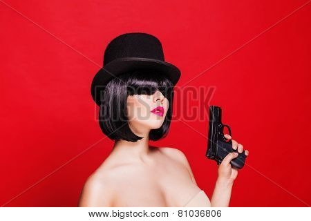 fashion beautiful model with pistol in hat cylinder, on red background