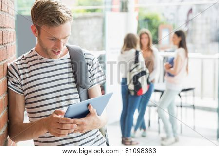 Handsome student smiling and holding tablet at the university