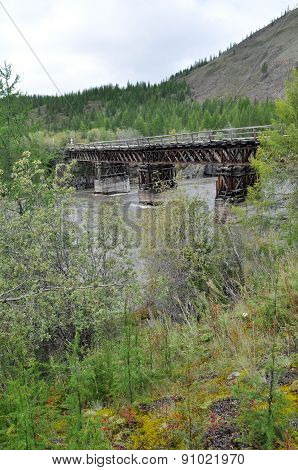 Wooden Bridge In Yakutia Across The Mountain River.
