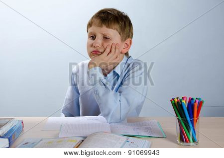 The student sitting in a classroom at a school desk, tired
