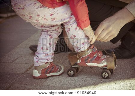 Father helping her little daughter to try on vintage roller skates. Old film photo style.