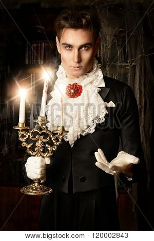 Handsome vampire man wearing elegant tailcoat stands in the old medieval castle. Halloween.