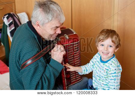 Little kid boy and grandfather playing music instrument
