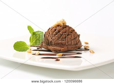 scoop of chocolate ice cream with mint and chopped nuts on white square plate - close up