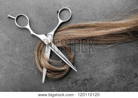 Hairdresser's scissors with strand of brown hair on grey background