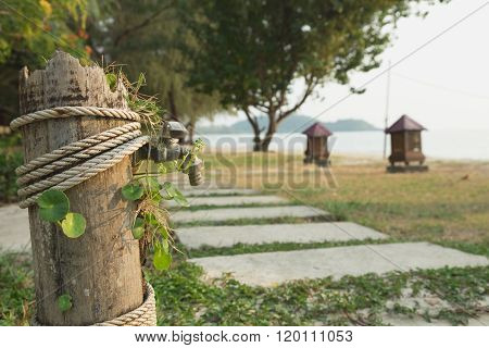 Old Tap Faucet With Old Wooden Cover And Rope On Stone Pathway On Grass Near Beach Wooden Lamp Sand