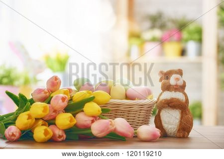 Happy Easter! Easter background with colorful eggs in basket, yellow and pink tulips and rabbit. Easter decoration with rabbit and eggs. Easter symbols: Bunny and eggs.