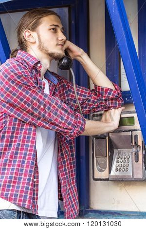 Young man talking on public phone.