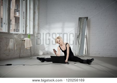Female dancer sitting on floor using laptop computer and mobilephone.