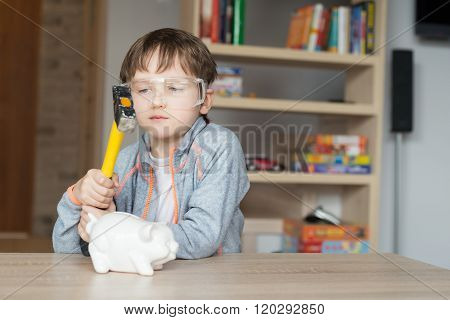 Little boy is going to break his piggy bank - proctective glasses on his eyes