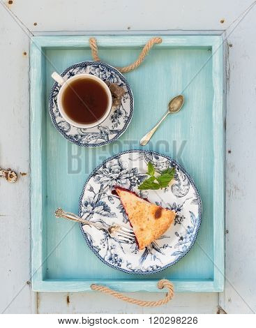 Piece of double crust plum pie and black tea in vintage porcelain cup, blue wooden tray. Top view .