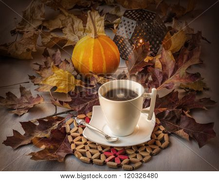 Cup of coffee on a wooden table with fallen leaves burning candle and pumpkins