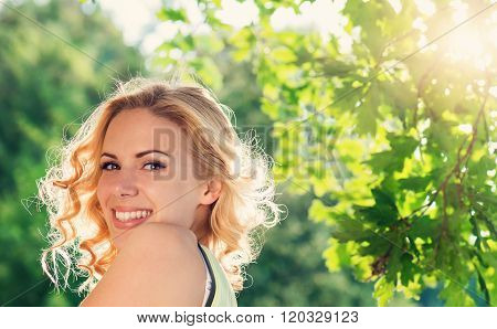 Blond woman, curly hair in green nature. Sunny summer