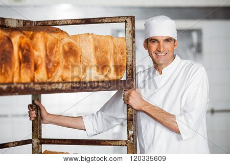 Mature Male Baker Standing By Bread Rack