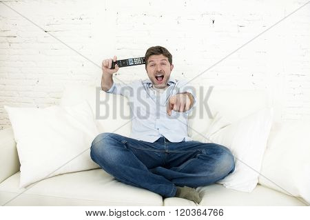 young happy man watching tv lying at home living room sofa with remote control looking relaxed smiling and laughing enjoying television program comedy movie or sitcom