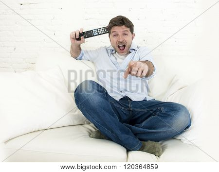 young happy man watching tv lying at home living room sofa with remote control looking relaxed smiling and laughing enjoying television program comedy movie or sitcom